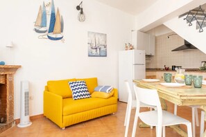 A bright yellow sofa, a dining table with chairs, a kitchen area, and a fireplace.