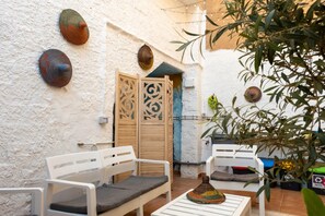 A courtyard with white walls, a wooden door, and two white chairs with cushions.