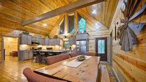 Una cabaña espaciosa de madera con una gran mesa de comedor, una zona de cocina y un rincón de estar acogedor.
