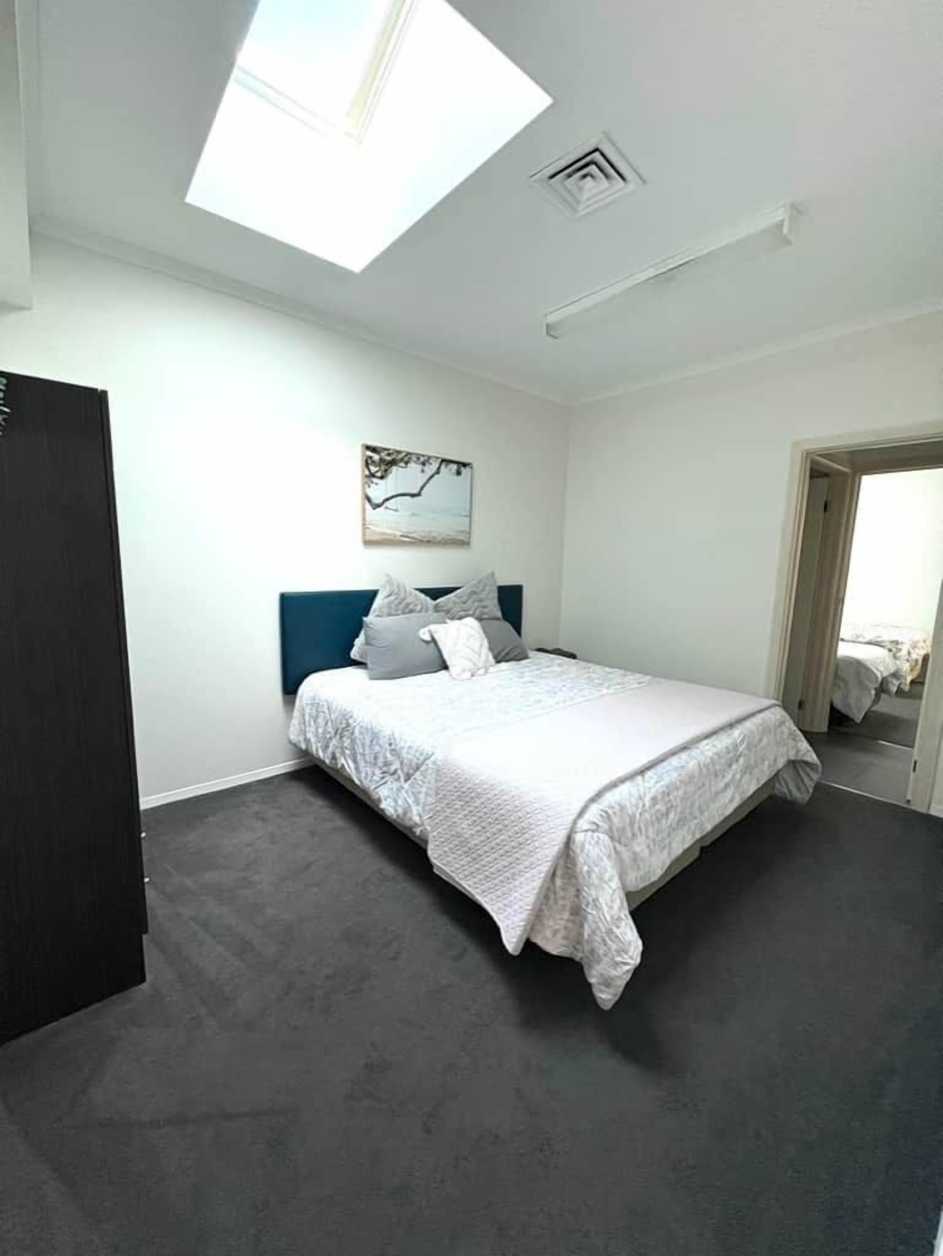 Ein Schlafzimmer mit Bett, einem dunklen Kleiderschrank, einem Oberlicht und einem Bild an der Wand.