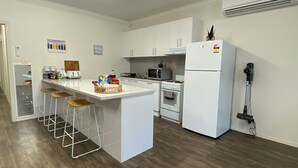 A modern kitchen with white cabinetry, a central island with stools, a microwave, stove, and a refrigerator.