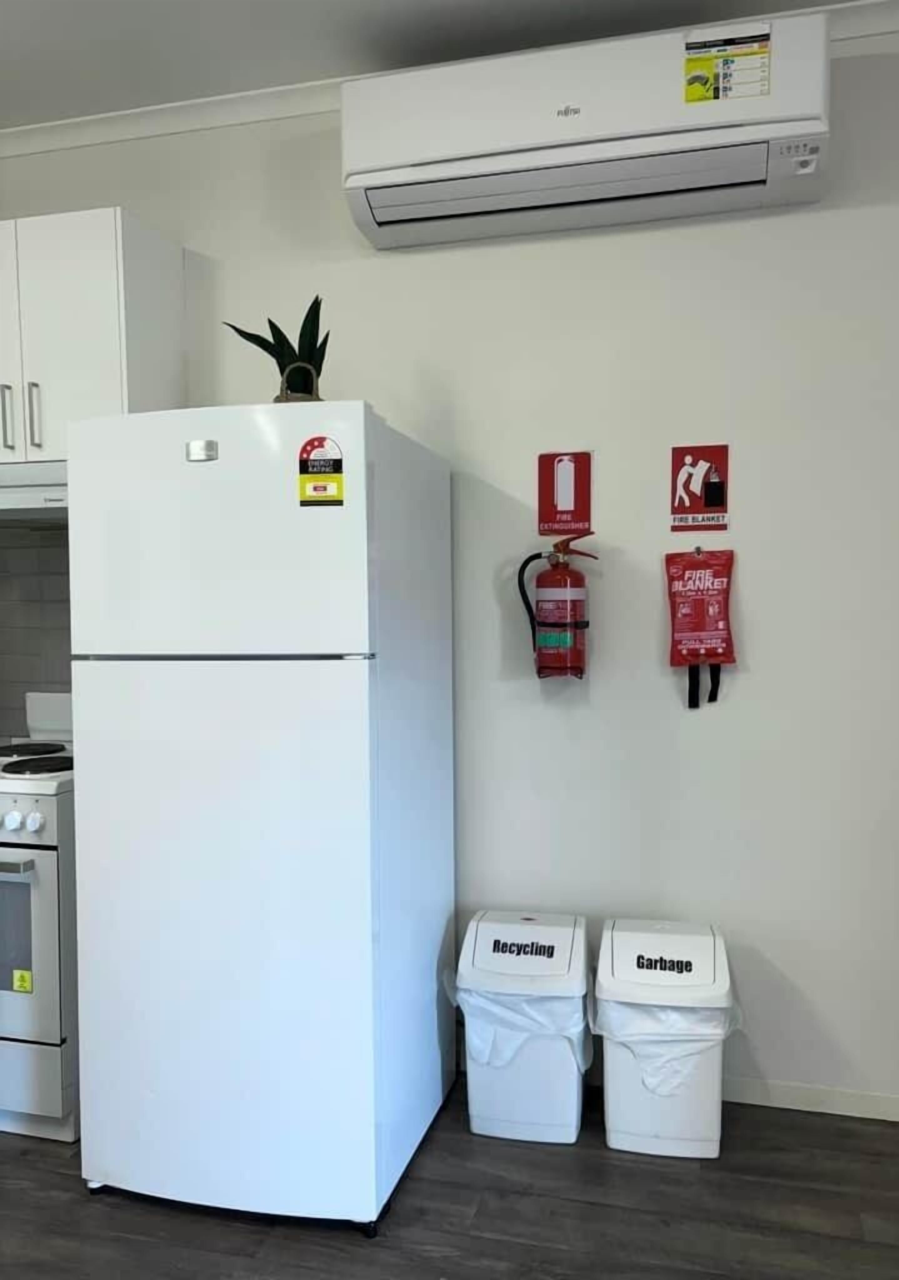 Eine Küche mit einem weißen Kühlschrank, einem Herd und zwei Mülleimern, auf denen 'Wertstoffe' und 'Restmüll' stehen.