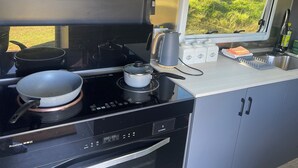 Ett litet, praktiskt kök med en spis, kastruller, en vattenkokare och ett fönster med utsikt över grönområden.