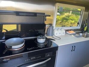 Una kitchenette compacta con estufa, ollas, hervidor y una ventana con vistas a la vegetación.