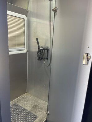 Un espacio de ducha compacto con ducha, manguera y una ventana con persianas.