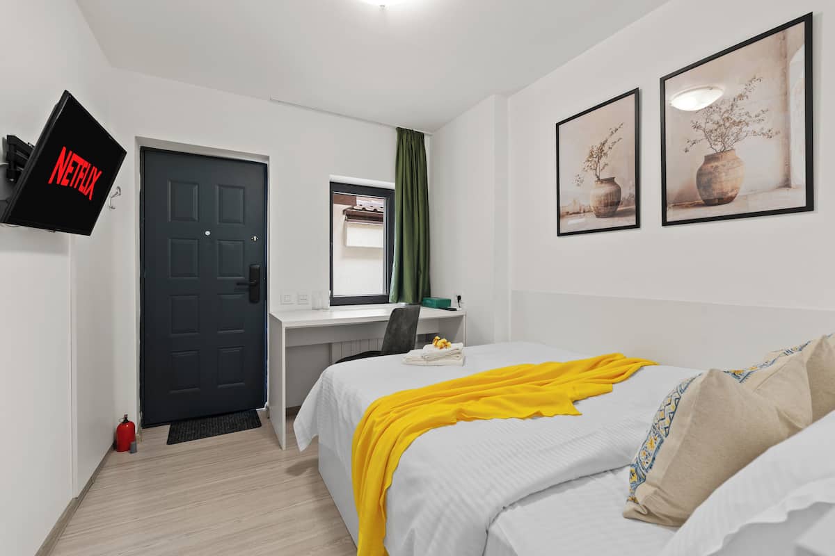 Ein Hotelzimmer mit Bett, Schreibtisch, Wandfernseher und zwei gerahmten Bildern an der Wand.