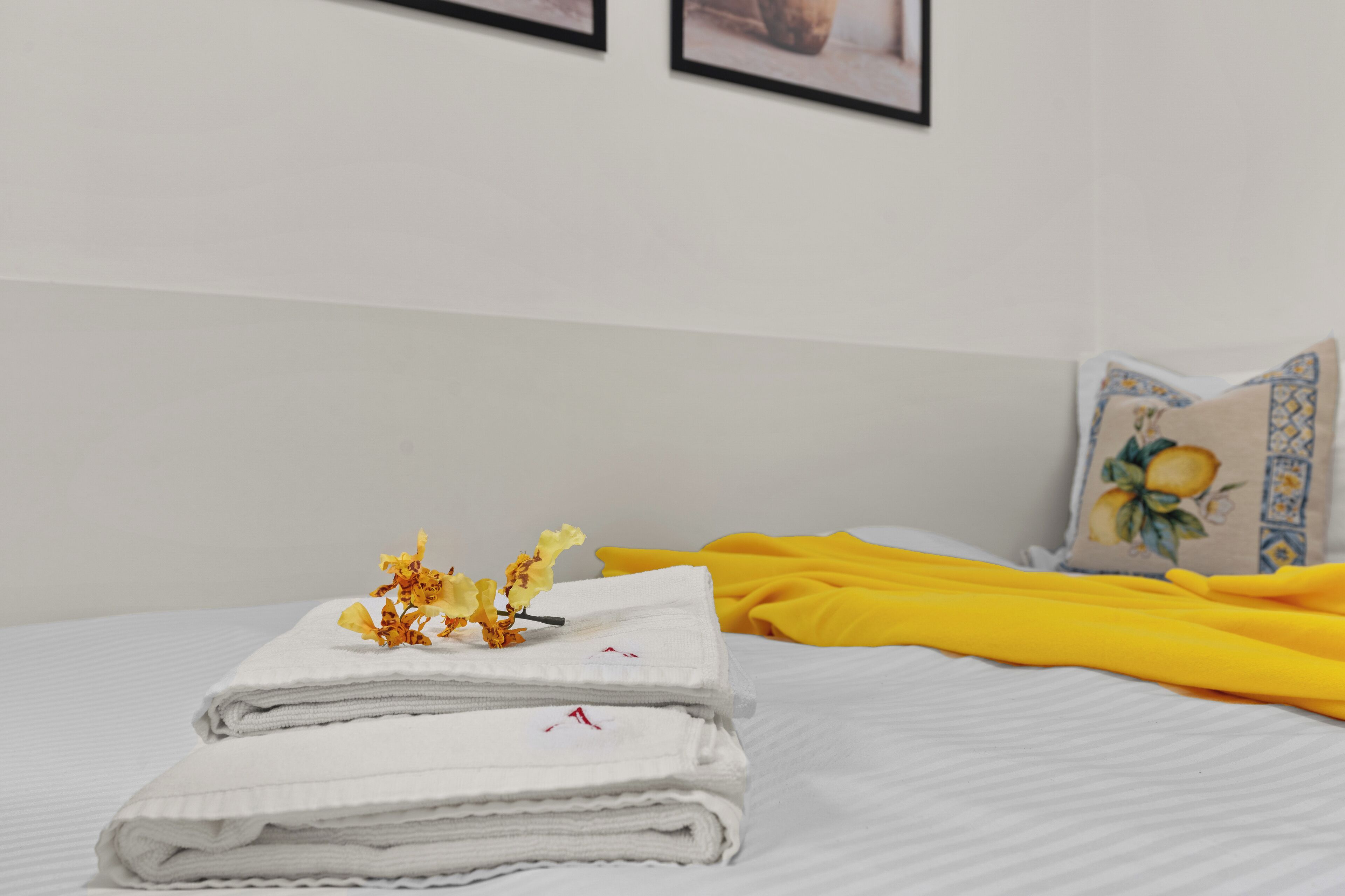 A neatly made bed with white linens, a yellow blanket, and a pillow with a floral design.