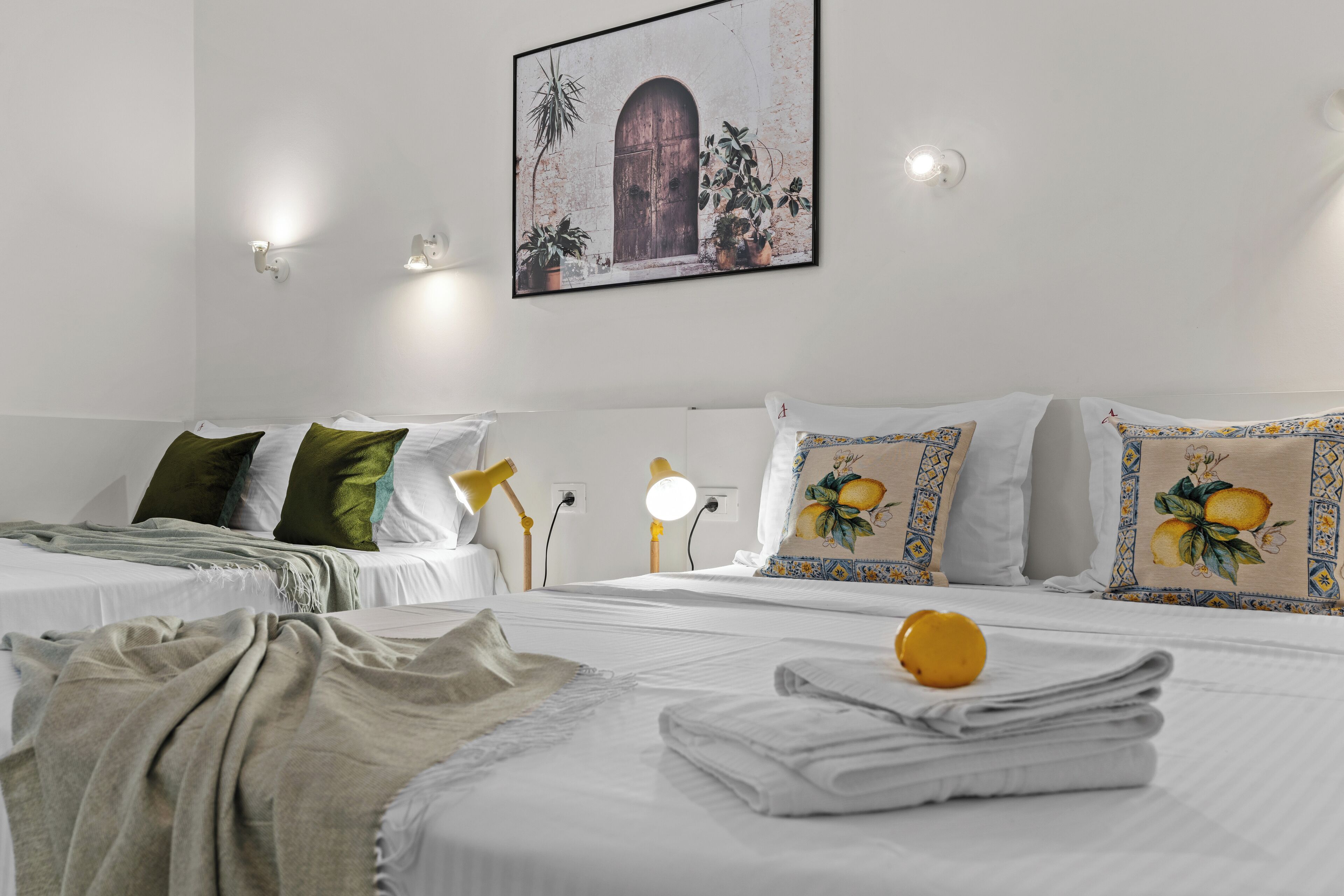 Une chambre d’hôtel avec deux lits, du linge de lit blanc, des oreillers verts à motifs, un tableau accroché au mur et des lampes de chevet.