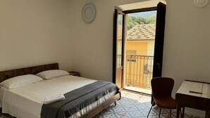 A bedroom with a bed, a table, a chair, and a balcony with a view of the outside. - Maripetra B&B (Sangineto)