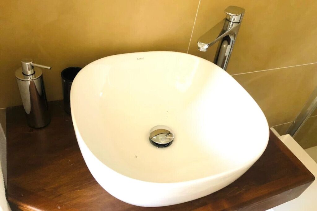A white oval sink with a chrome faucet and a soap dispenser on a wooden countertop.