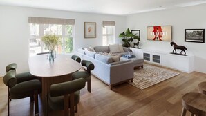 Un salon moderne avec une table à manger ronde, un canapé gris et un mur blanc orné d’œuvres d’art.