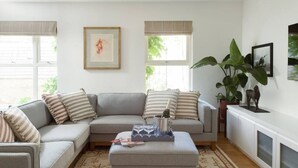 Un salon avec un canapé d’angle gris, une table basse avec un plateau, un tapis à motifs et une grande plante verte.