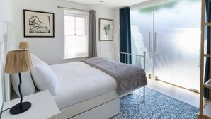 Une chambre à coucher avec un lit, une table de chevet, une lampe, une fenêtre et une vue sur l’extérieur.