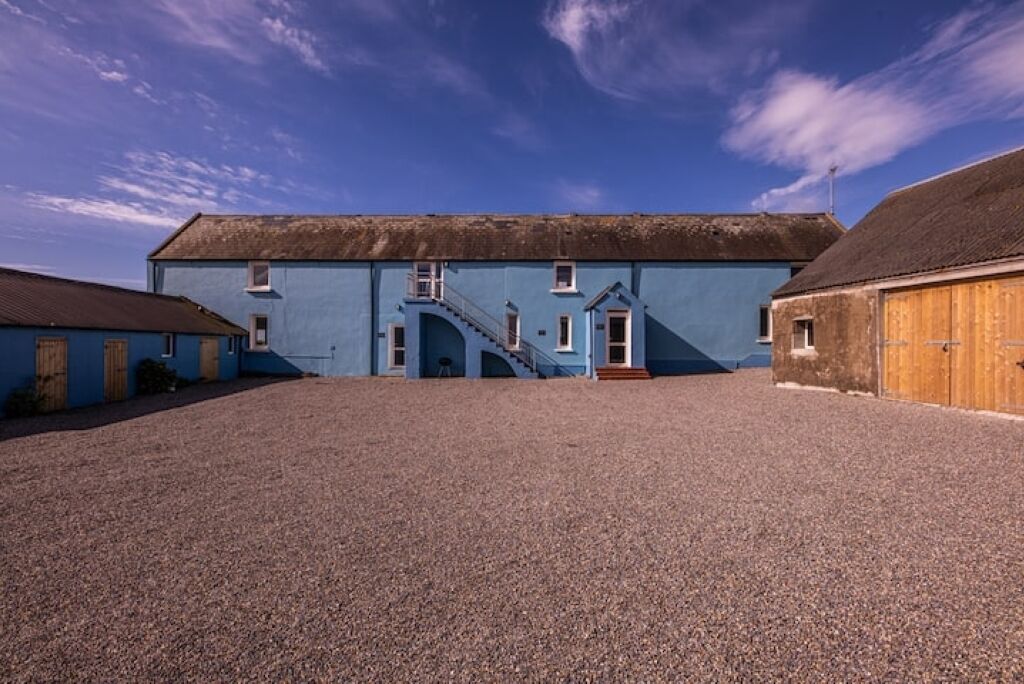 A large building with a blue facade, a central staircase, and a gravel courtyard.