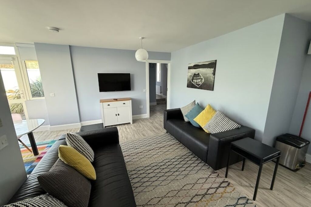 A modern living room with a black sofa, a small table, and a TV on a white cabinet.