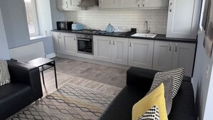 Eine moderne Küche mit weißen Schränken, einer schwarzen Arbeitsplatte und einem eingebauten Backofen. Ein schwarzes Sofa mit gemusterten Kissen und ein kleiner Tisch mit einer Lampe stehen hier.