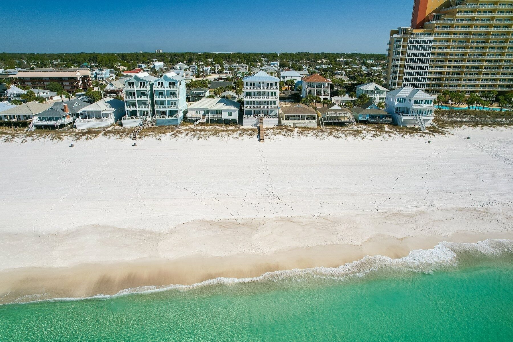 A beachfront property with multiple-story buildings, a sandy beach, and clear turquoise waters.
