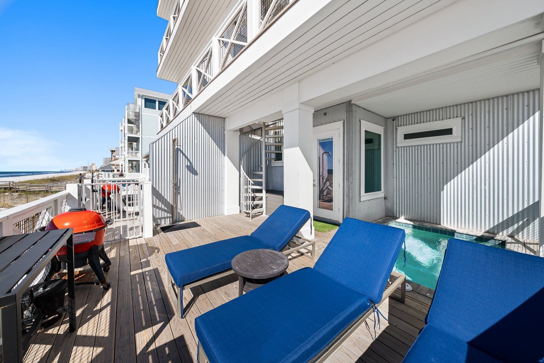 Eine Terrasse mit blauen Liegestühlen, einem kleinen Tisch und einem Poolbereich.