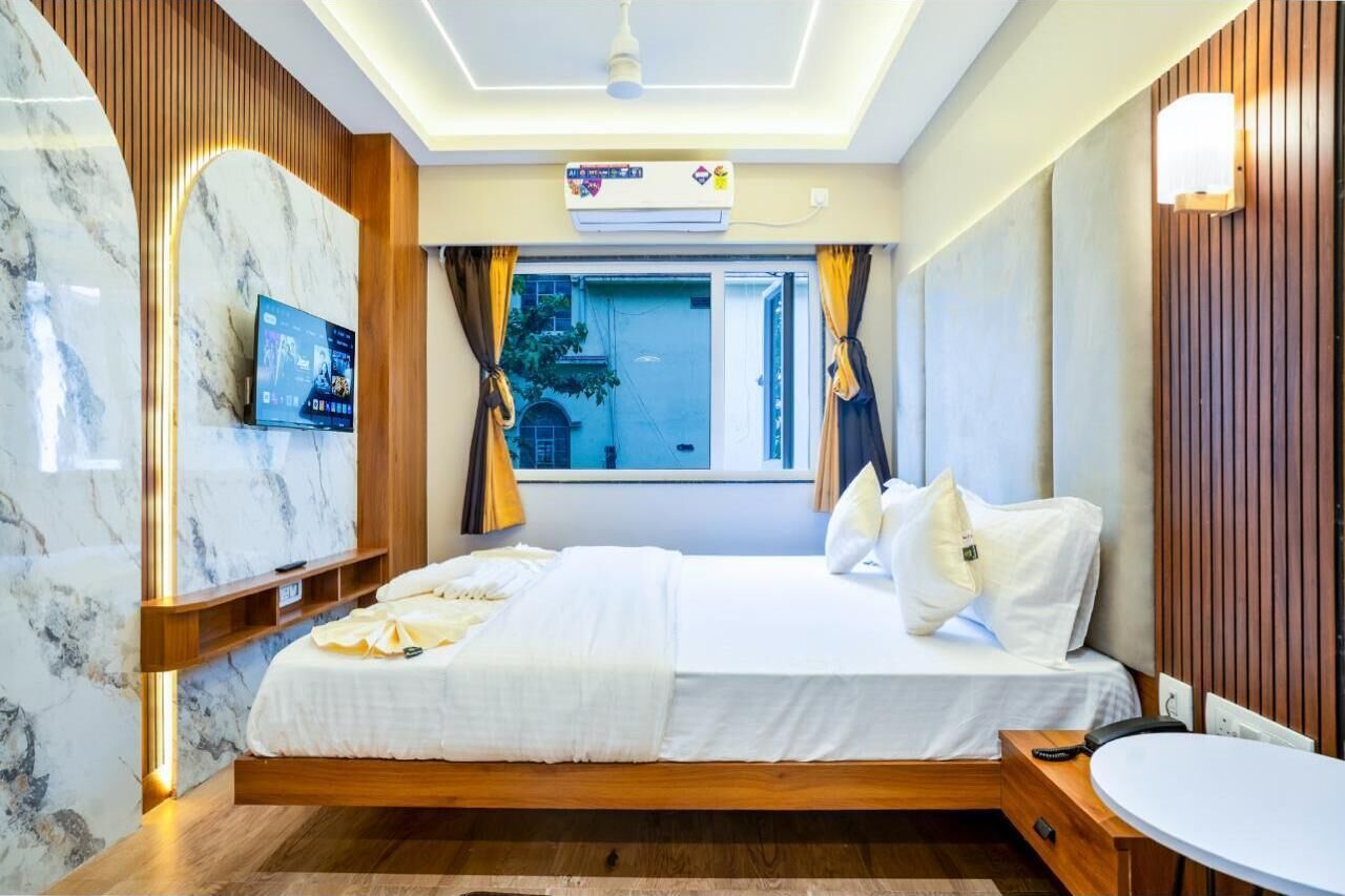 A modern hotel room with a bed, a TV, a desk, and a window with curtains.