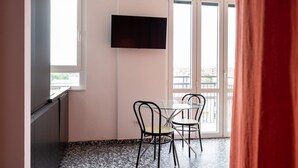 Ett rum med ett glasbord och stolar, en platt-TV som är monterad på väggen och stora fönster med utsikt över byggnaderna utanför.