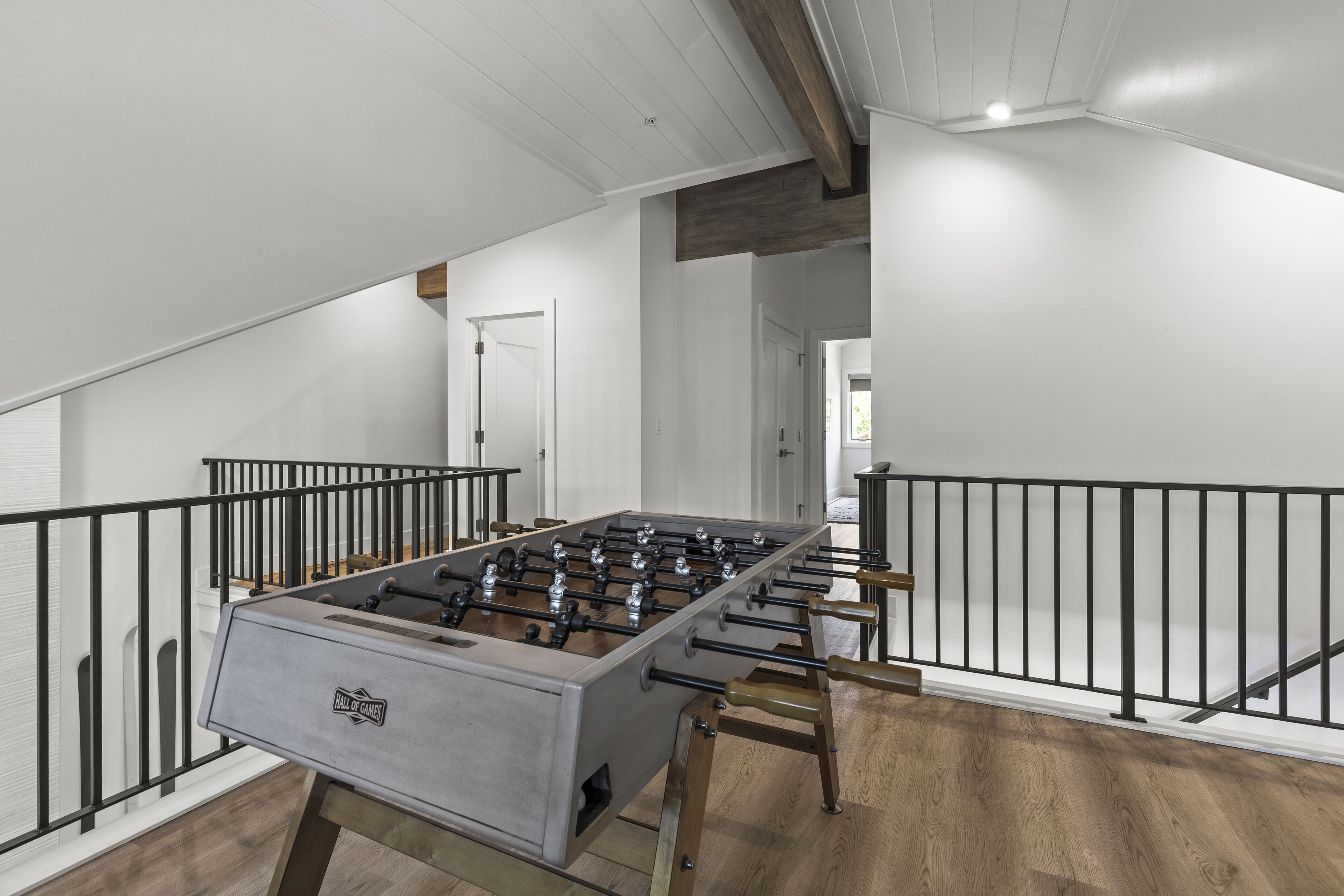 Une pièce spacieuse équipée d’un baby-foot, dotée d’un plancher en bois et d’un escalier avec des rampes noires.