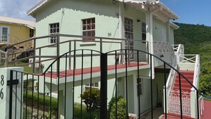 A two-story building with a red and white exterior, numbered 86, featuring a gated entrance and a small porch area. - Peaceful 2BR/1BA modern home, perfect for a laid-back Caribbean getaway (Gros Islet)