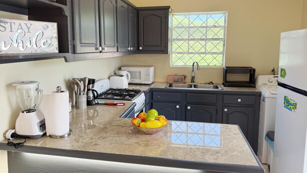 A kitchen with dark cabinets, a countertop with a blender, toaster, and a bowl of fruit. - Peaceful 2BR/1BA modern home, perfect for a laid-back Caribbean getaway (Gros Islet)
