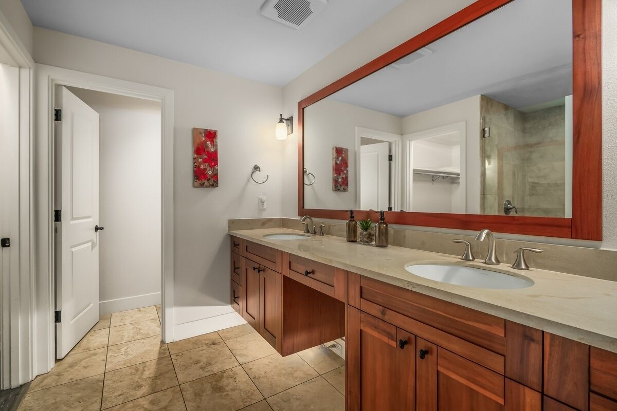 A bathroom with two sinks, wooden cabinets, a large mirror, and a tiled floor.
