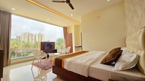 Habitación de hotel con una cama grande, televisión, escritorio y vistas a palmeras y edificios.