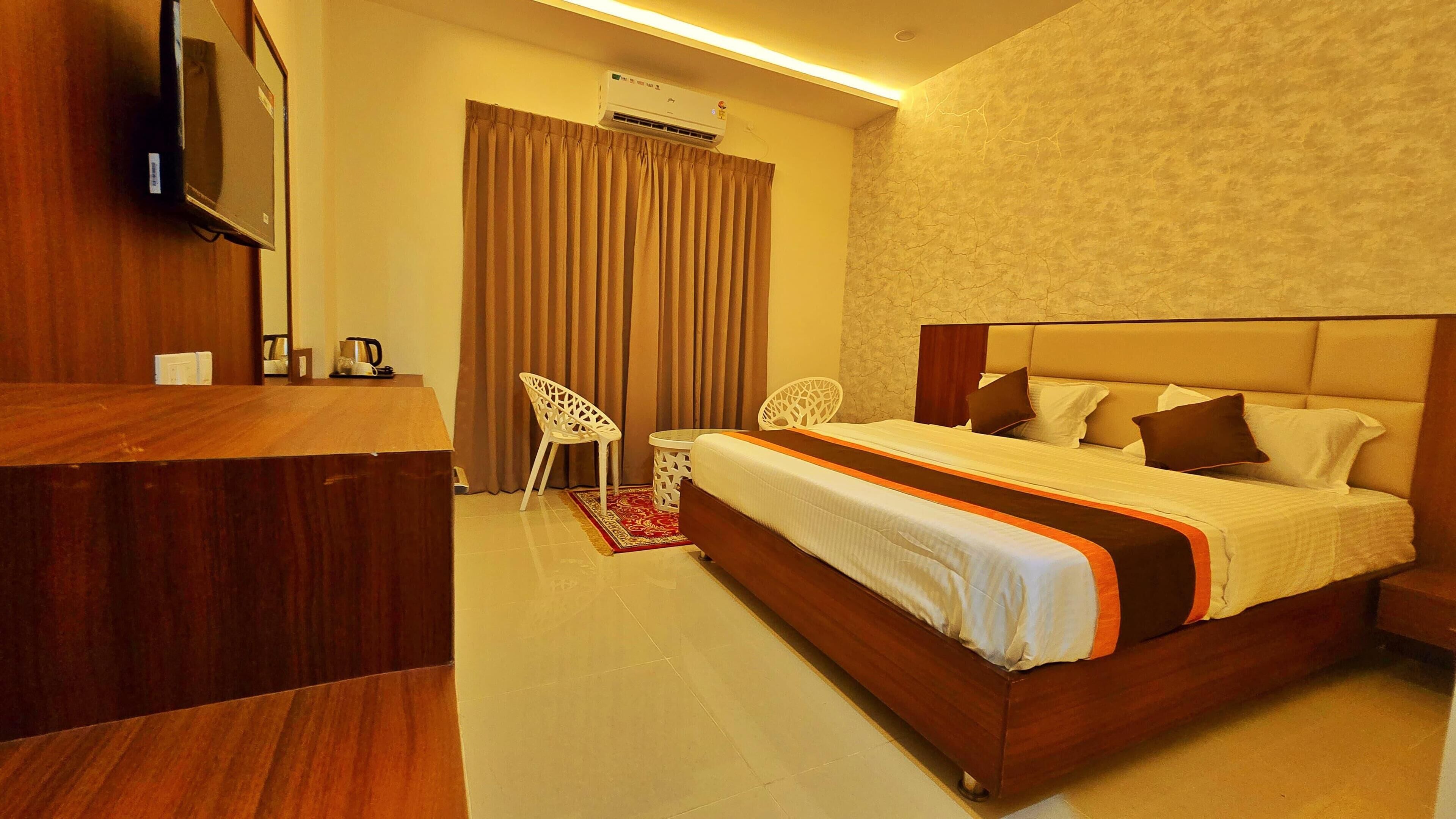 A hotel room with a wooden desk, a bed with a headboard, a TV mounted on the wall, and an air conditioning unit.