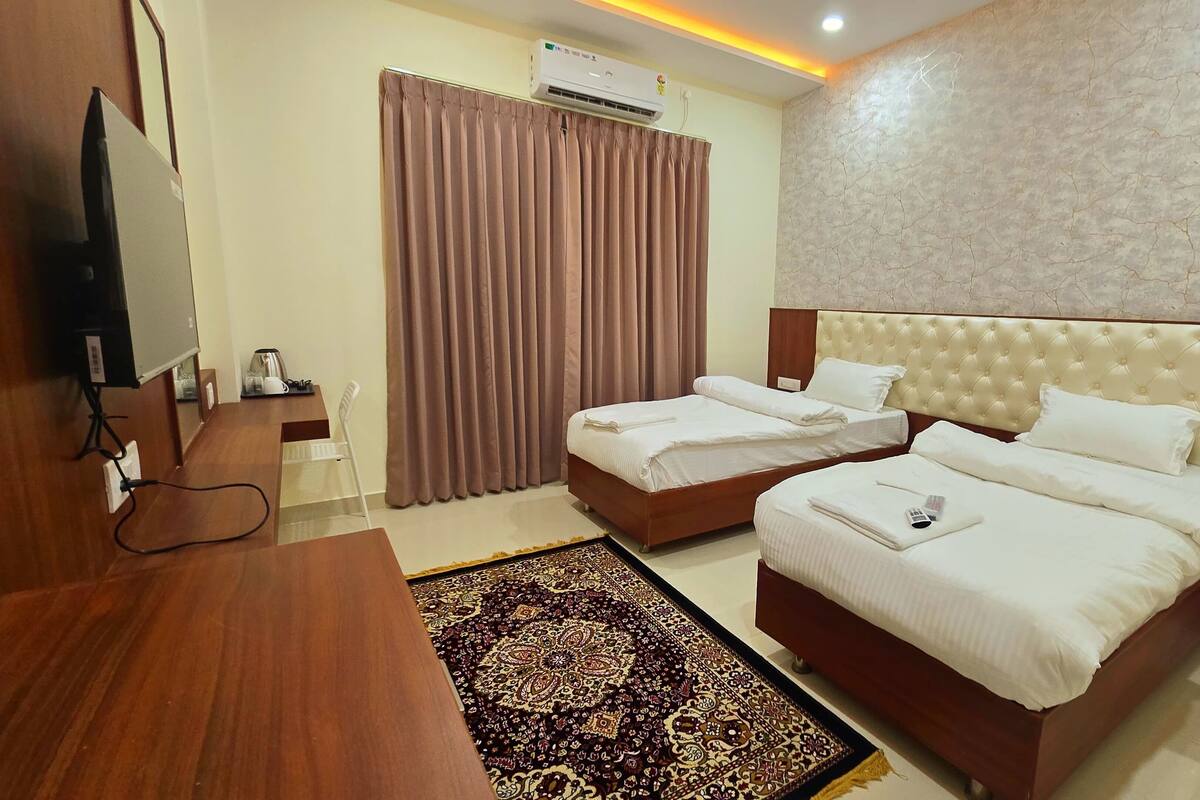 A hotel room with two beds, a TV, a desk, and a patterned rug.