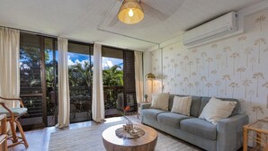 A living room with a grey sofa, a round wooden coffee table, and a large window with curtains. - Maui Vista 2223 1 Bedroom Condo (Kihei)