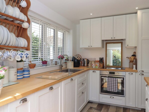 A modern kitchen with white cabinets, a wooden countertop, and a built-in oven. - Rowan (Brixham)