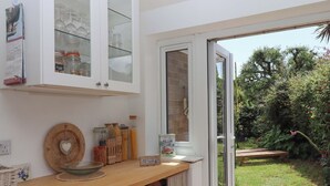 Een keuken met een houten aanrecht, open kastjes en uitzicht op een tuin door een glazen deur.
