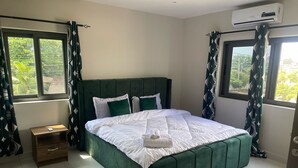 Une chambre à coucher bien rangée, avec un lit recouvert d’un tissu vert, du linge de lit blanc et une petite table de chevet en bois.