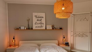 Une chambre à coucher avec un grand lit, des lampes de chevet, une étagère murale décorée de divers objets et un panier suspendu.