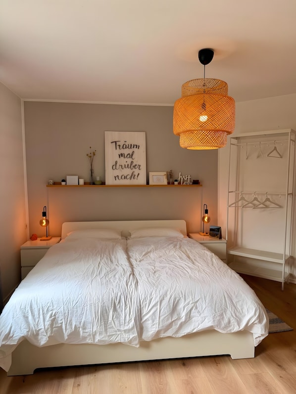 A bedroom with a large bed, bedside lamps, a wall-mounted shelf with decorative items, and a hanging basket.