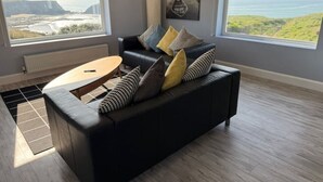 Una sala de estar moderna con un sofá de cuero negro, una mesa de centro redonda y vistas al mar a través de amplios ventanales.