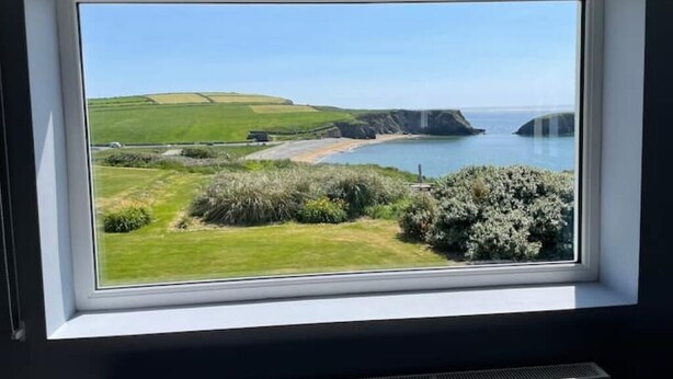 Vista desde una ventana de un paisaje costero con campos verdes, una playa y acantilados.