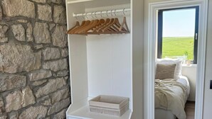 A bedroom with a stone wall, a white wardrobe with a mirror, and a view of a green field through a window. - Gite 2 in the heart of the countryside (Chimay)