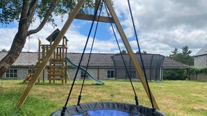 A trampoline in a grassy yard with a wooden swing set and a slide in the background. - Gite 2 in the heart of the countryside (Chimay)