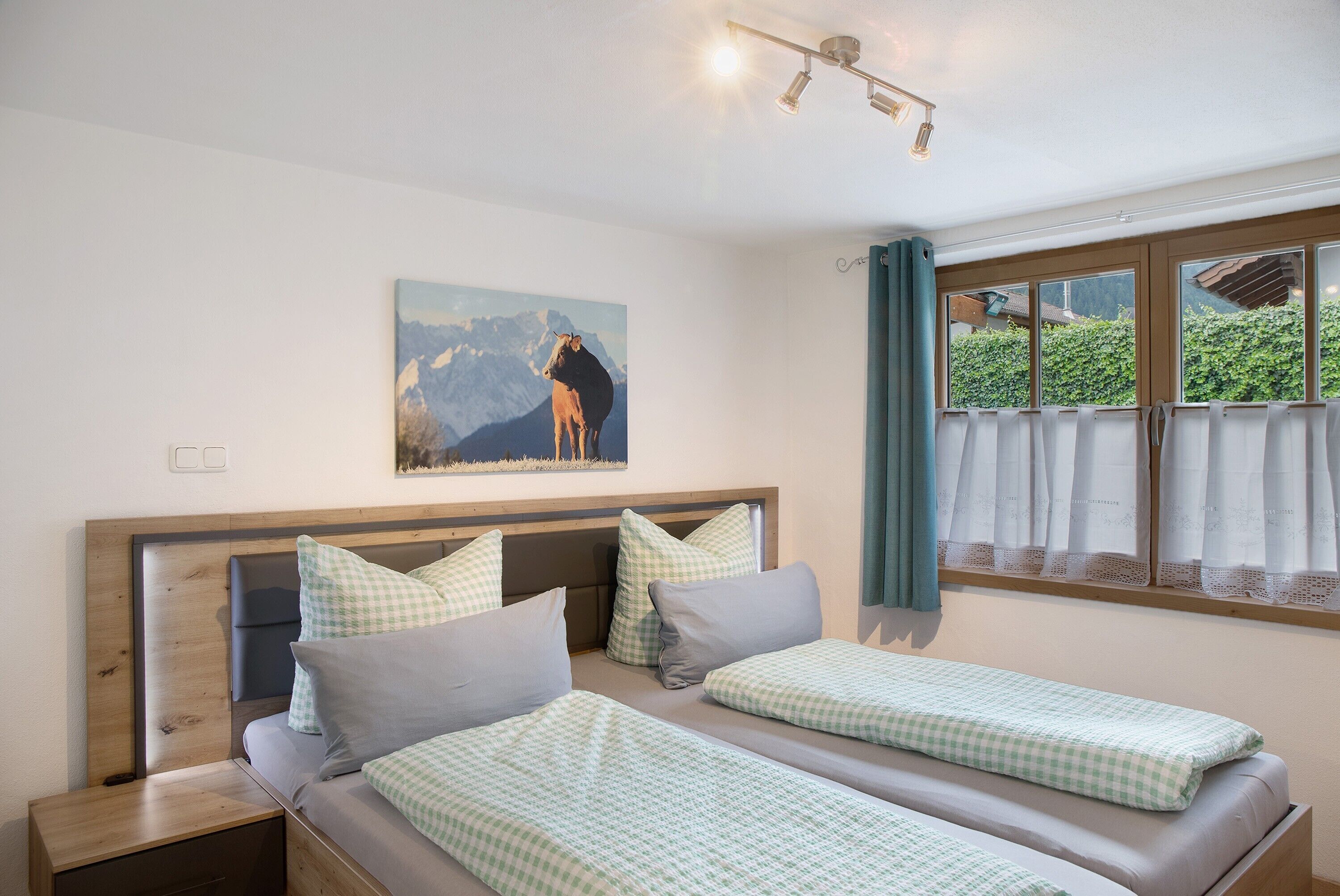 Een kamer met twee bedden, een houten hoofdeinde, een schilderij van een paard en een raam met gordijnen.