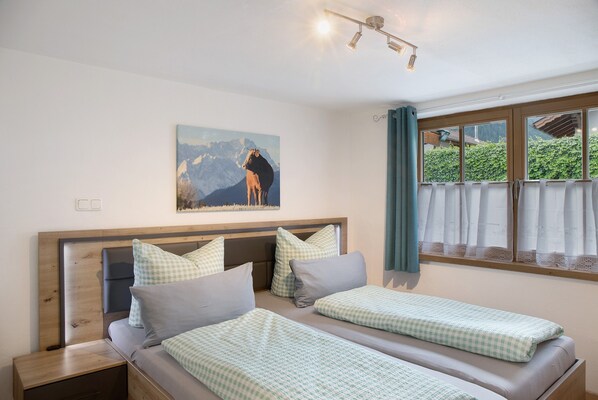 A room with two beds, a wooden headboard, a painting of a horse, and a window with curtains.