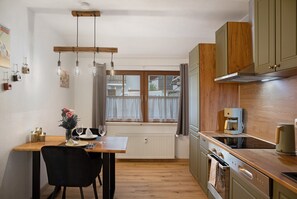 A kitchen with wooden cabinets, a dining table with chairs, a hanging light fixture, and a window with curtains.