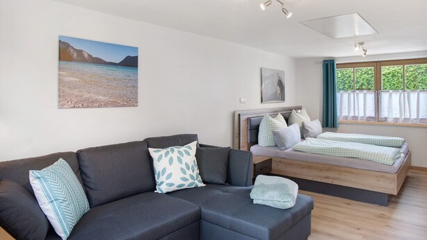 A modern room with a sofa, a bed, a window with curtains, and artwork on the walls. - Holiday Apartment 'Wankblick' with Mountain View, Private Terrace and Wi-Fi (Farchant)