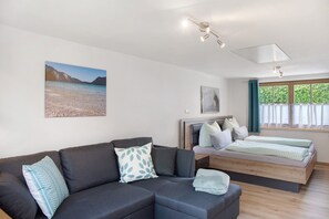 A modern room with a sofa, a bed, a window with curtains, and artwork on the walls.