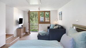 A bedroom with a bed, a sofa, a television, a dresser, and a window with a view of greenery. - Holiday Apartment 'Wankblick' with Mountain View, Private Terrace and Wi-Fi (Farchant)