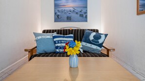 A room with a wooden table, striped sofa, and a framed picture of a beach scene.