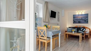 A room with a dining table, chairs, a sofa, a TV, and a painting on the wall.