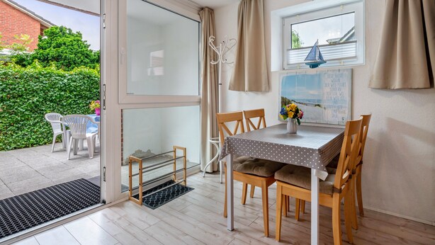 A dining area with a table and chairs, a coat rack, and a window with curtains.